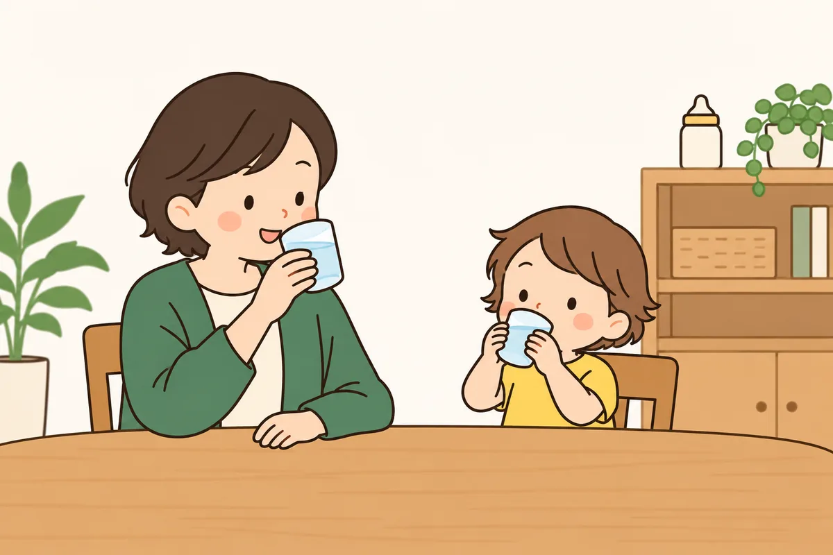 子どもが両手でふつうのコップを持って飲み、横で大人がほほえんでいる。